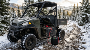 Side-by-side UTV on a snowy trail with a jump starter plugged into a quick-connect tender lead