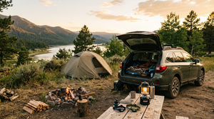 Car camping setup at sunset with tent, camp table, headlamps, lantern and a hatchet by the fire ring